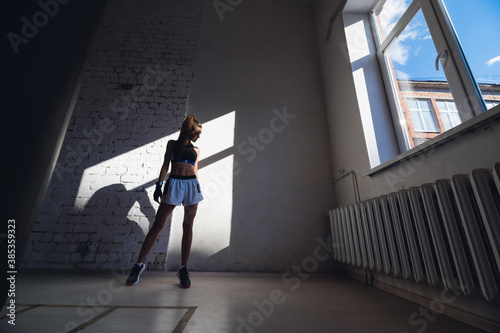A pretty long-haired brunette of athletic build stands against a brick wall in the loft