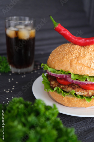 Delicious burger with red and hot peppers on top, soda in the background. Black background. advertising photo. 