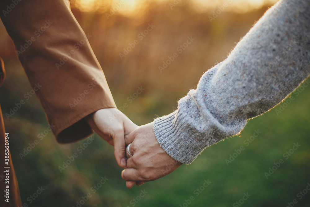 Couple gently holding hands in warm sunset light in autumn field, close up. Conceptual image Couple gently holding hands in warm sunset light in autumn field, close up. Conceptual image