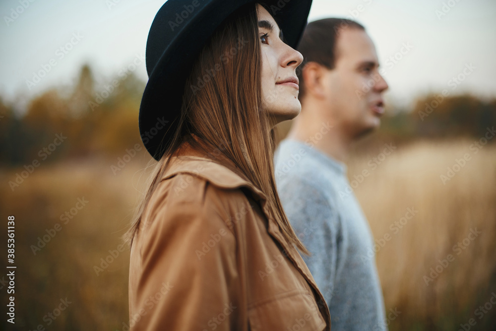 Stylish couple walking among grass and herbs in autumn field in sunset Stylish couple walking among grass and herbs in autumn field in sunset