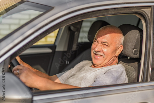 Elderly man driving a car, looking at the camera. driving or old age concept. 