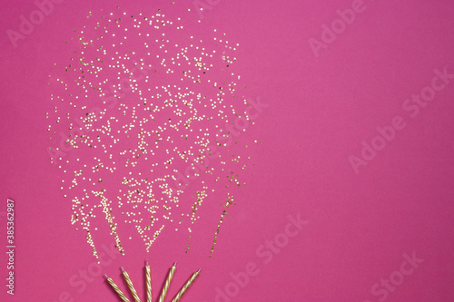 Candles are burning with golden confetti. Festive, Christmas and New Year composition on a pink background. Horizontal orientation, top view. Copy space.