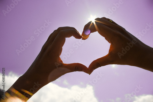 Heart symbol from hands on the blue sky background, Female hands in the shape of a heart on a background of bright sun