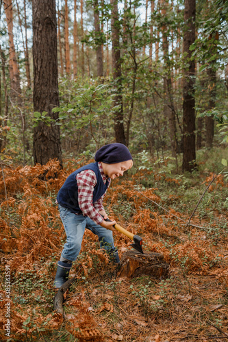 Little boy in the autumn forest. A boy with an ax near a tree. Woodcutter hold ax. Standing in the forest with axe.
