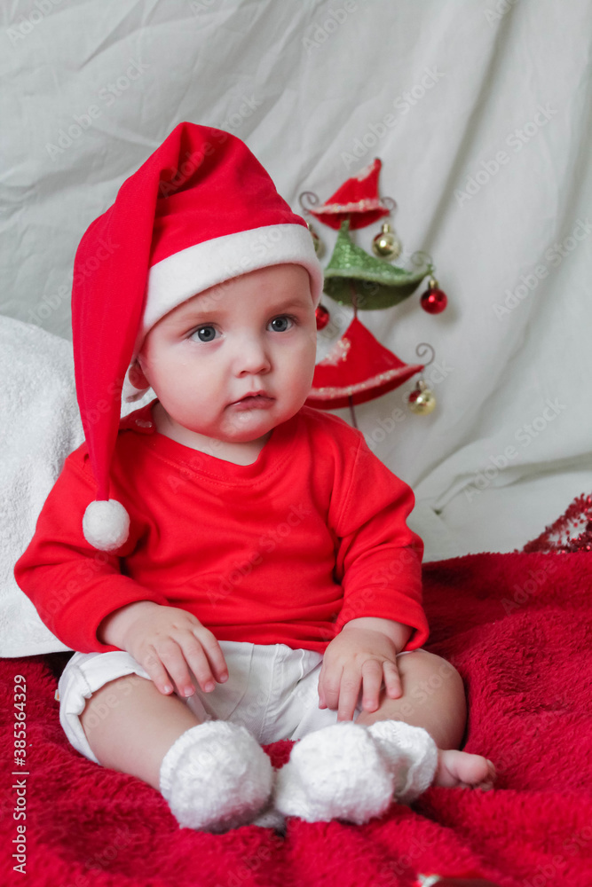 A beautiful little child is celebrating Christmas. New year holiday. Baby in a Christmas costume is happy sitting on the floor A beautiful little child is celebrating Christmas. New year holiday. Baby in a Christmas costume is happy sitting on the floor