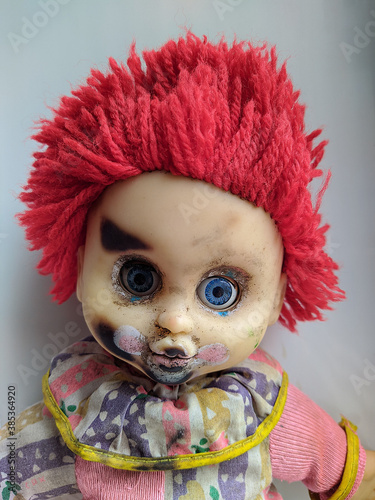 scary and old battered clown doll with burnt face and red hair on the white background photo