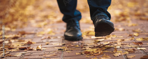 Men boots walking on the sidewalk strewn with autumn leaves