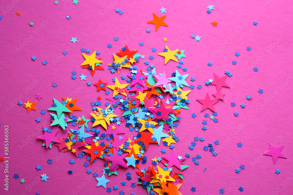 Party decorations on a pink background. Multicolored little and big plastic confetti stars. Blue tiny glitter stars. Festive pattern. Spree. Festival. Birthday. Christmas.