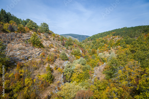 Amazing fall colors of the trees in the forest in a valley, surrounded by hills and distant mountain peak under a blue sky
