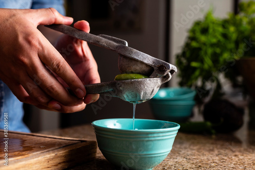 Man squeezing lime with a metal squeezer into a bowl. photo