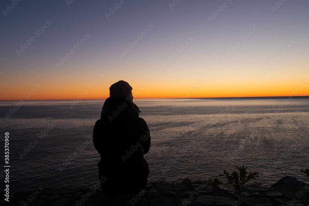 Back view of a young woman admiring the sunrise at Cap Bon-Ami, in the Forillon national park, Canada