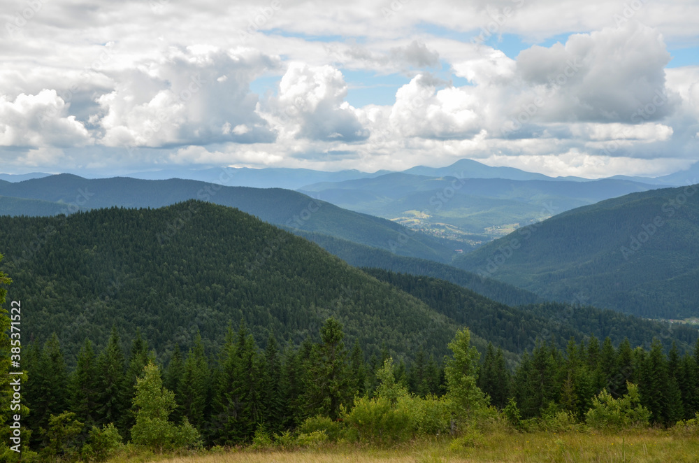 Carpathian covered forest and village, mountain ridge on background. Cloudy day in Carpathians, Ukraine