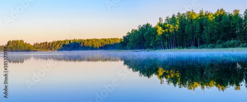 Panoramic view sunrise at Lake Haukivesi with mirror reflection in the water. Fog over the water.