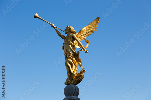 Side view of golden statue of angel blowing in trumpet seen against bright blue sky, Saint-Augustin-de-Desmaures, Quebec, Canada