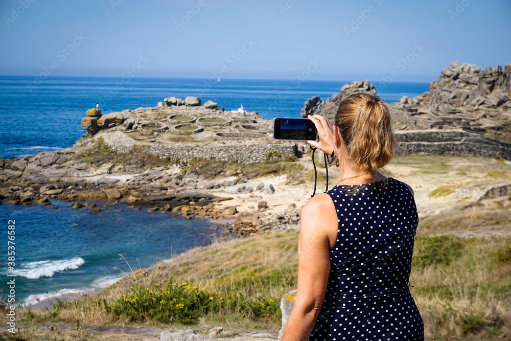 Woman photographing the Castro de Baroña in the province of La Coruña Woman photographing the Castro de Baroña in the province of La Coruña