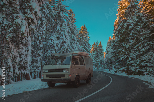 Canvas-taulu Front view of an adventure vintage retro campervan or off road vehicle on a snowy road during colorful sunset or sunrise
