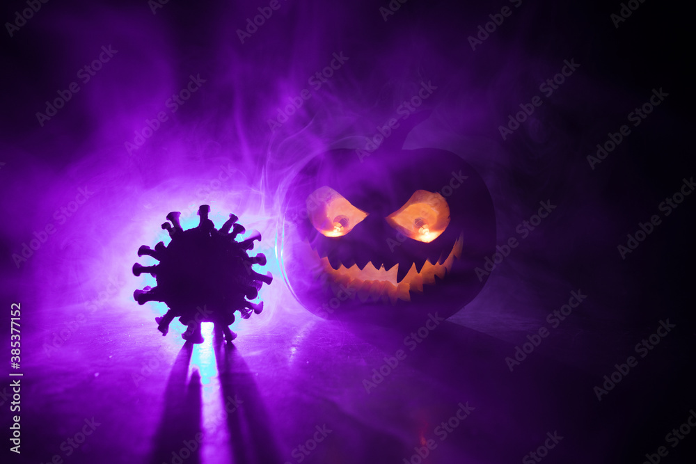 Fototapeta premium Halloween during Corona virus global pandemic concept. Glowing pumpkins and Covid novel on dark with thematic spooky decorations. Halloween pumpkin on foggy backlight.
