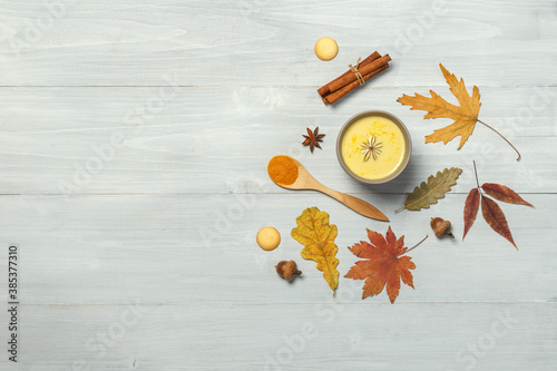 Golden milk with turmeric and spices on a light wooden surface with bright dry autumn leaves. Top view with space