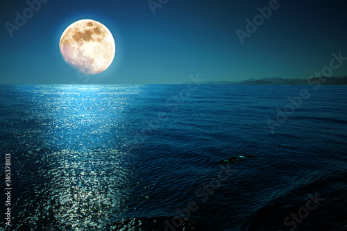 Full moon with reflections on a calm sea at midnight.