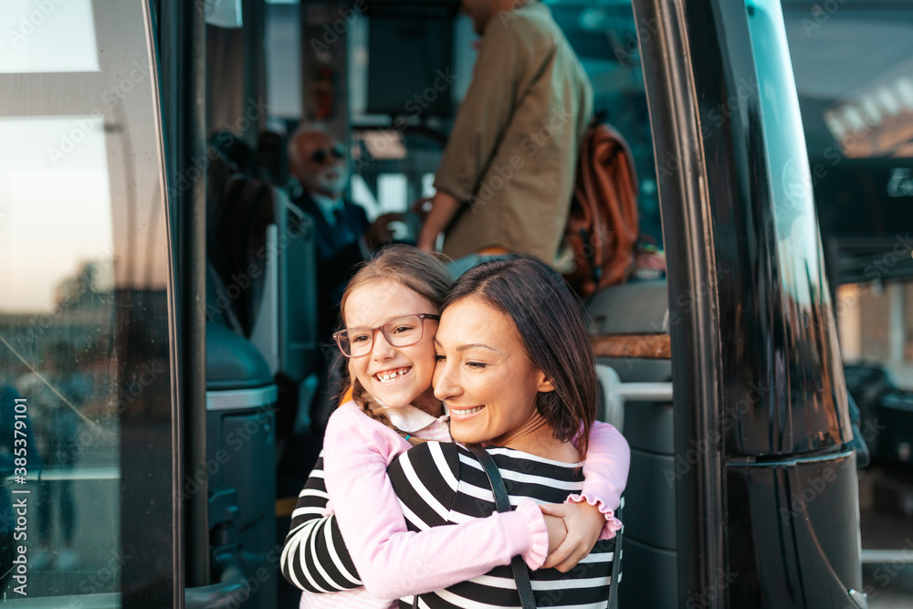 A mother hugs her daughter in front of the bus before her trip. - obrazy, fototapety, plakaty 