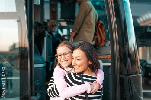 A mother hugs her daughter in front of the bus before her trip.