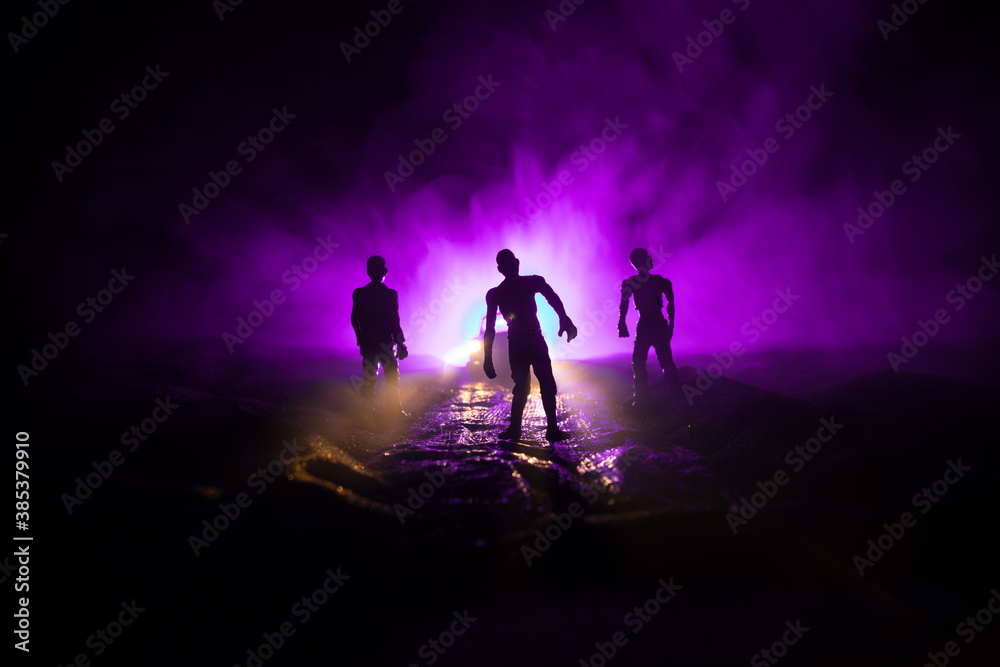 photo of a car stopped on the road lighting up a zombies. Silhouette terrible zombie night near the car. Miniature decoration.