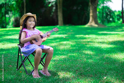 little asian girl sitting on chair and playing ukulele in the park
