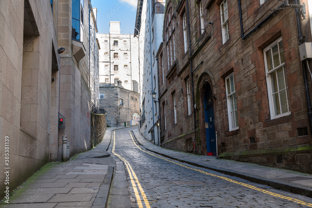 Empty narrow cobled street lined with stone buildings on a sunny winter day. Edinburgh, Scotland.