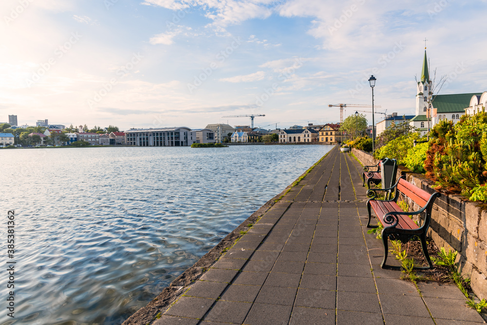 Footpath lined with empty wooden benches along the shore of a lake in a city centre. Reykjavik, Iceland.