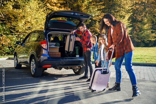 Canvas Print Joyful family helping each other to unload auto's trunk from carton boxes and su
