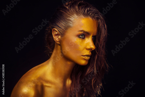 Close-up portrait of beautiful young model with glowing golden skin. Gold, jewellery, accessories, care products, cosmetics concept. Golden skin woman face.