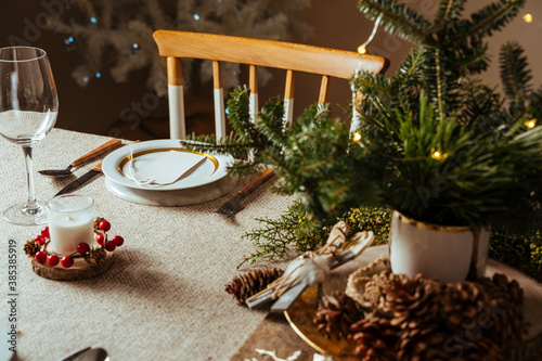 Homely christmas table setting, decorated with pine branches and rustic tablecloth in the living room of home tree lit background