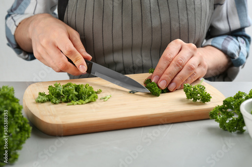 Woman cutting curly parsley at light grey table, closeup