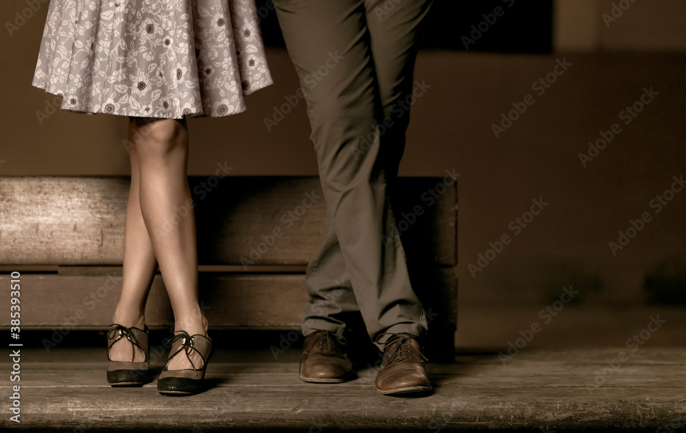 Crossed legs of a couple standing on a wooden bench.