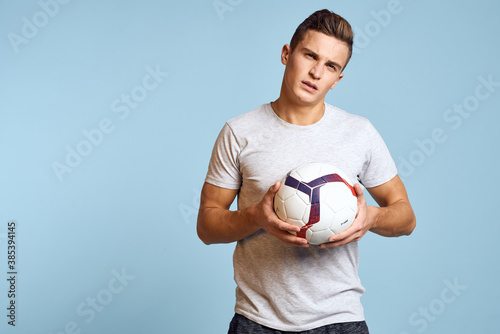 Happy guy with soccer ball in hand on blue background plays soccer cropped view © SHOTPRIME STUDIO