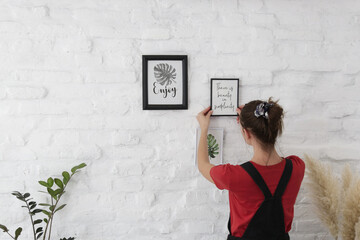 Woman arranging picture frames on wall in new house, diy home improvement concept