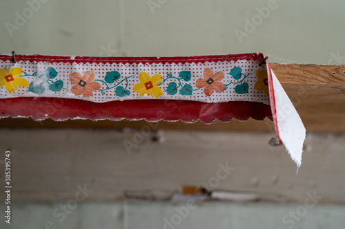 Torn, peeling wallpaper border is ripped against the wall. Useful for abstract backgrounds. Floral, colors of red, green and yellow photo