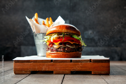 Hamburguesa doble con papas a la francesa montada sobre madera en fondo gris con vista a 0 grados