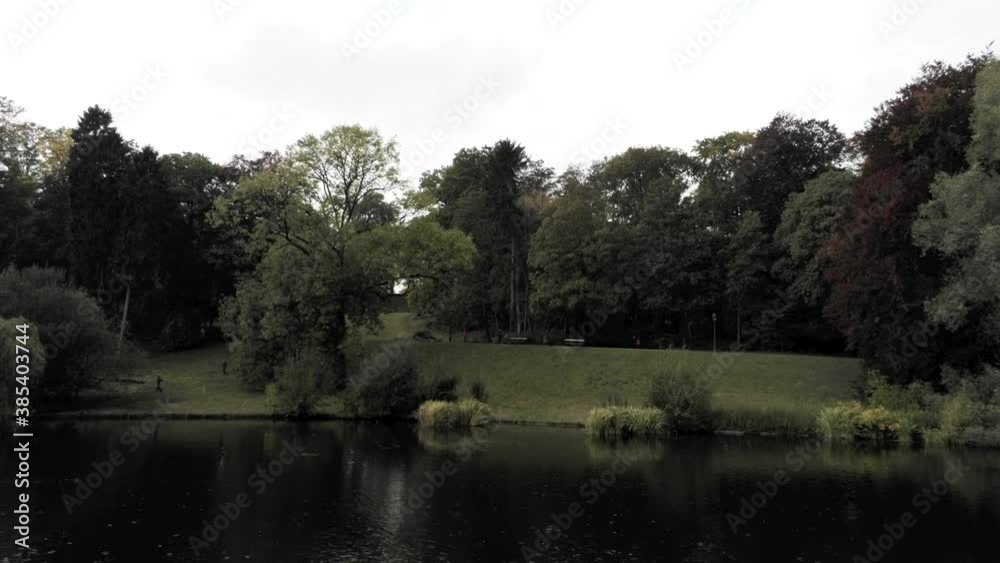 Raining Park Woods By The Green Grass Lake Surface In Brussels, Belgium. - Aerial - Approaching Shot Raining Park Woods By The Green Grass Lake Surface In Brussels, Belgium. - Aerial - Approaching Shot