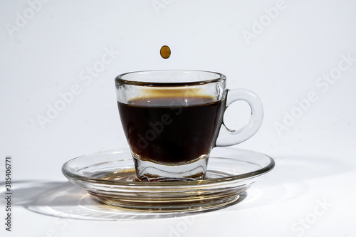 Coffee droplet on transparent glass espresso cup saucer full of liquid coffee on white background