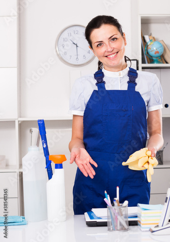 Cheerful female cleaning furniture in office with rag and cleanser photo