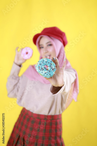 Smiling Young Woman Asian girl holding donuts. Young cheerful woman with donuts at studio yellow background, copy space. Sweet life and sweet food.