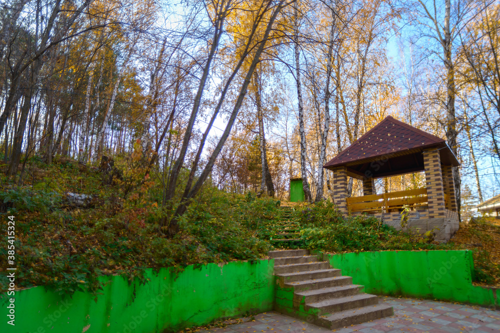 Stone gazebo in the autumn forest with yellow fallen leaves.