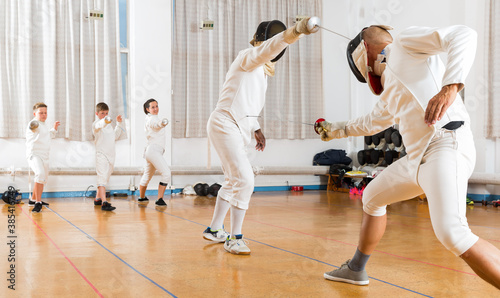 Adults and teens wearing the fencing uniform practicing with foil in a gym