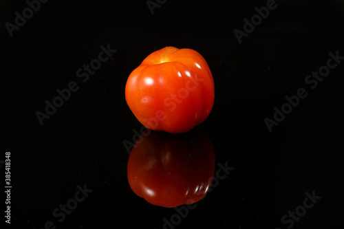 Fresh ripe small shiny red tomato on black background photo