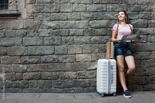 Traveling happy female standing with suitcases on stone wall background.