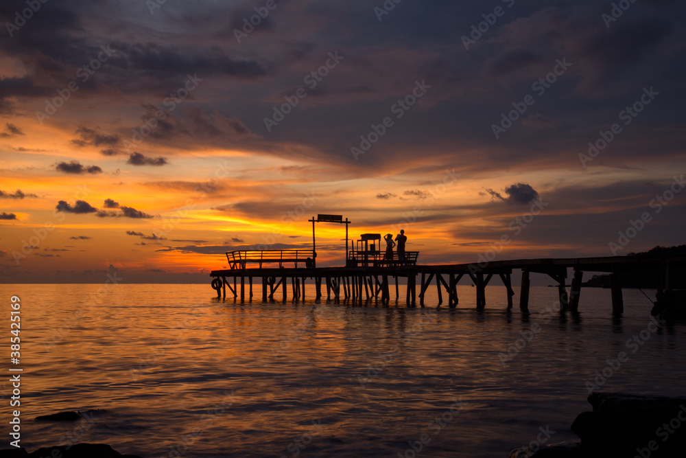 The scenery of the silhouette of the couple taking a photo on the wood bridge in sunset time in Koh Kood island, Trat province, Thailand.