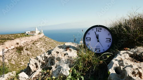 Time is running out. Clock ticking showing twelve o' clock against travel destination. Mesa Roldan lighthouse, Cabo de Gata Nijar, Andalusia Spain. Holidays travelling and adventure concept. photo