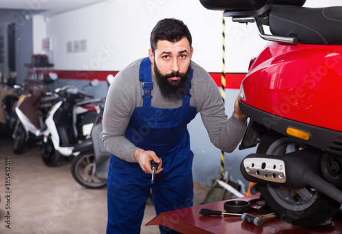 Positive male worker repairing scooters in motorcycle workshop