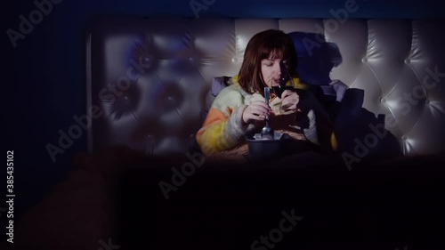 woman in the evening with wine and ice cream lies on the bed and watches tv